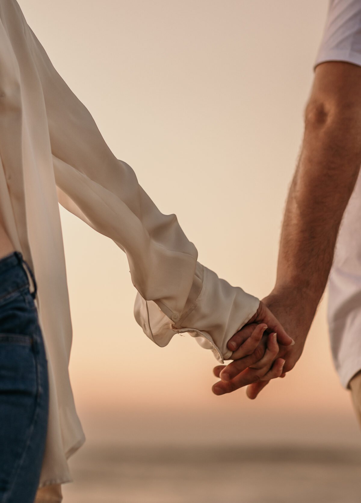 couple qui se tient les mains en marchant sur la plage au coucher du soleil. Photographie lifestyle douce et romantique dans les Landes, France Photographie réalisée par Charlotte Marette