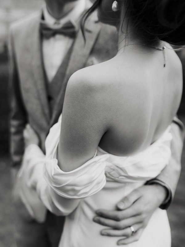 Couple marié s'enlaçant à Paris. La femme est de dos, photo de mariage romantique, élégante et intemporelle en noir et blanc. Photographie réalisée par Charlotte Marette dans les galeries du Louvre à Paris, France